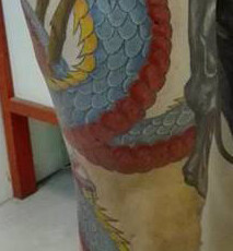 Tatouage d'un dragon en couleur s'enroulant autour de la jambe