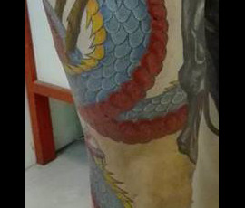 Tatouage d'un dragon en couleur s'enroulant autour de la jambe