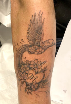 Tatouage d'un oiseau de style "fine art". Tatouage d'un oiseau de style "fine art" ou "fine work" avec des détails très fins de fleurs.